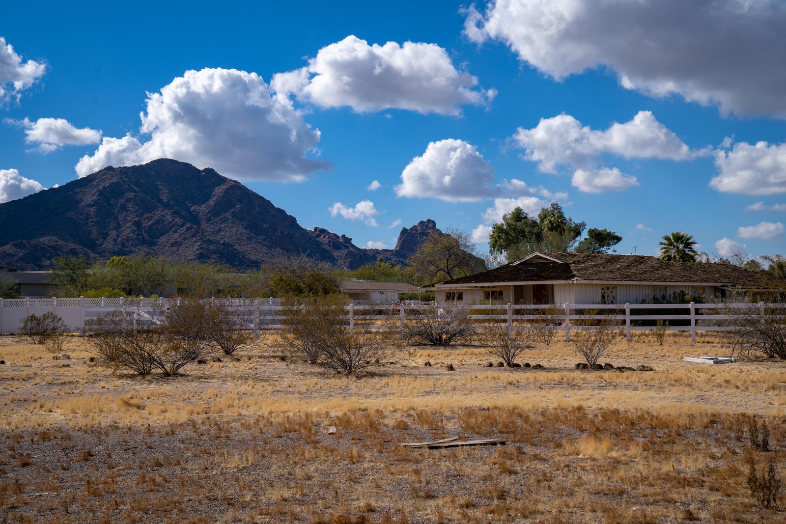 Single-story ranch home behind white rail fencing with desert scrub and mountain backdrop representing Florence