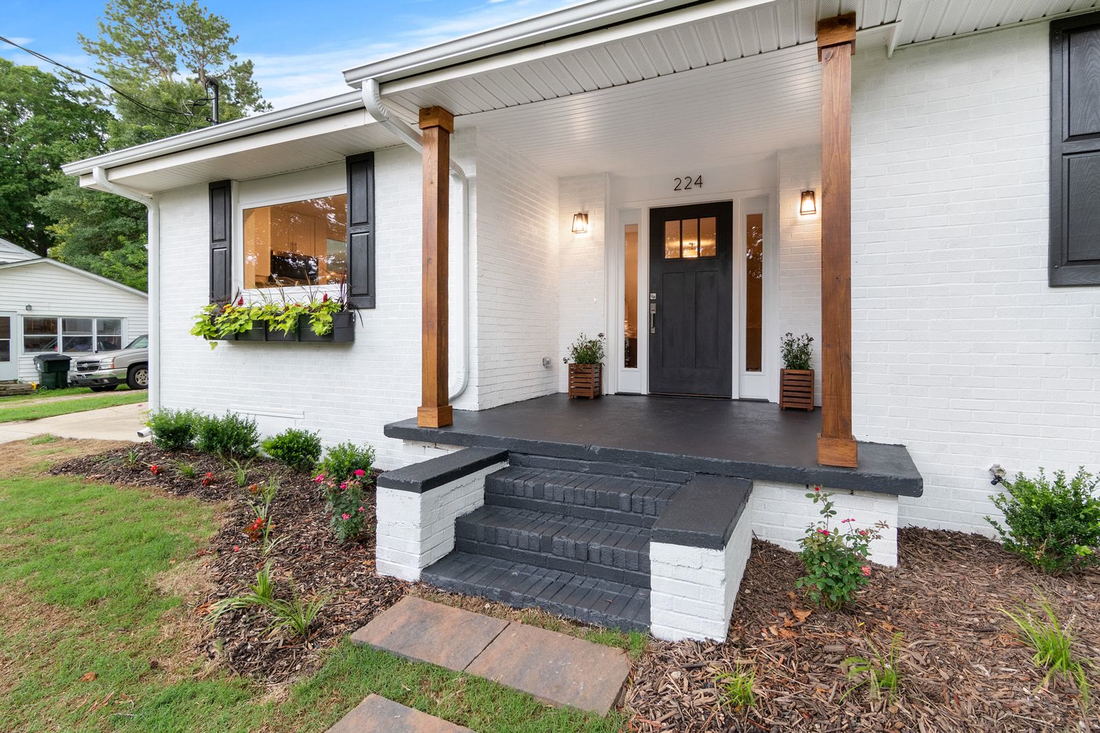 Modern farmhouse porch with white brick, wood columns, charcoal door, and black shutters